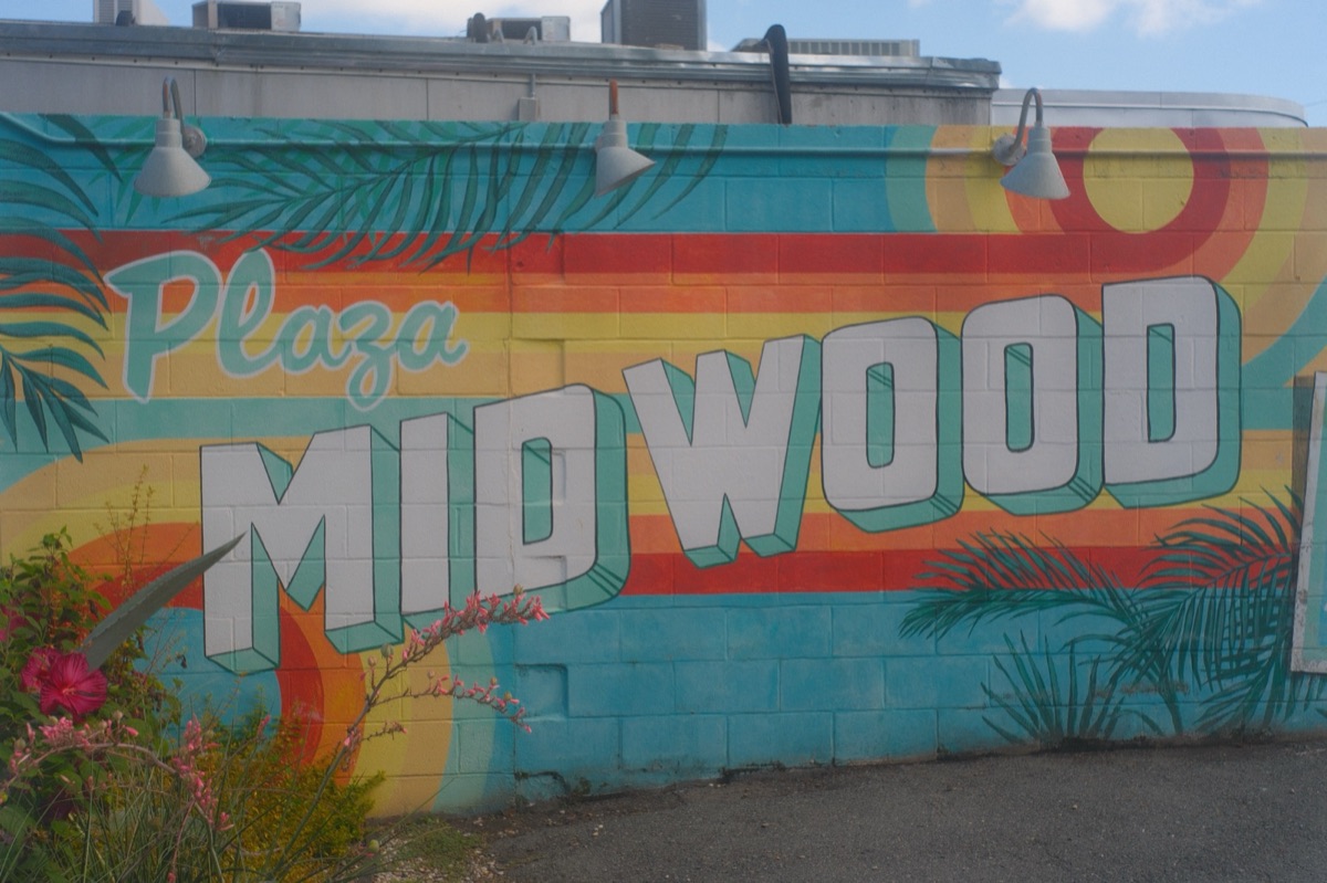 A bright retro mural reading Plaza Midwood in white block letters over teal, orange and red stripes